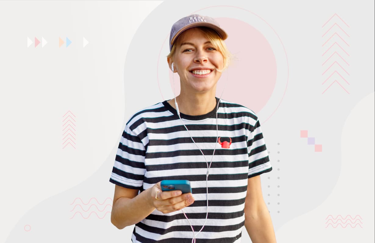 uśmiechnięta dziewczyna w koszulce w biało-czarne paski z słuchawkami w uszach trzyma telefon