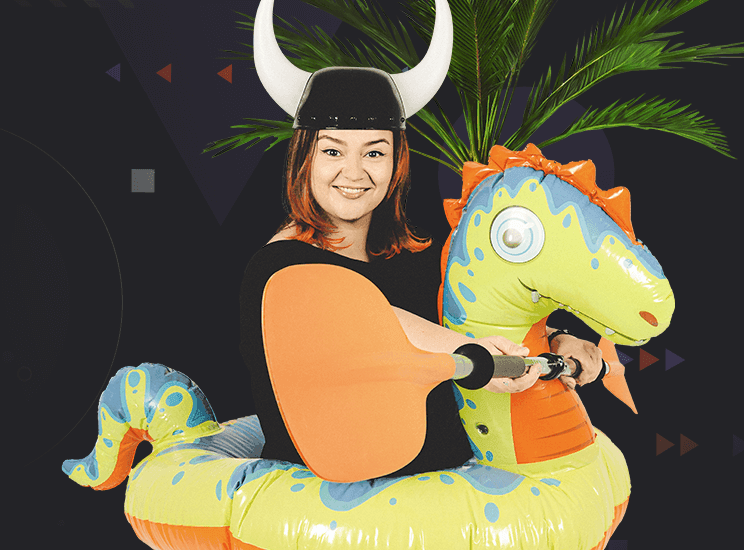 A smiling girl in a Viking helmet sits on an inflatable dinosaur holding a paddle in her hands