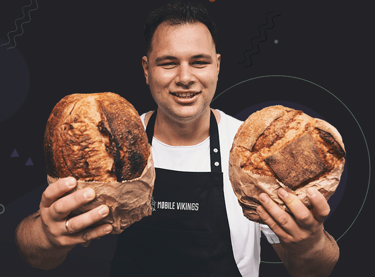 Smiling man in a Mobile Vikings apron holds two loaves of bread wrapped in paper