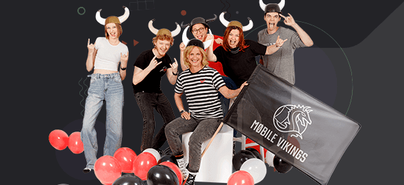 Group wearing horned helmets poses among balloons with a Mobile Vikings flag, flashing rock hand signs